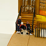 Model of a group of people with a boombox on a cardboard set with a door and boxes.