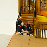 Model of a group of people with a boombox on a cardboard set with a door and boxes.