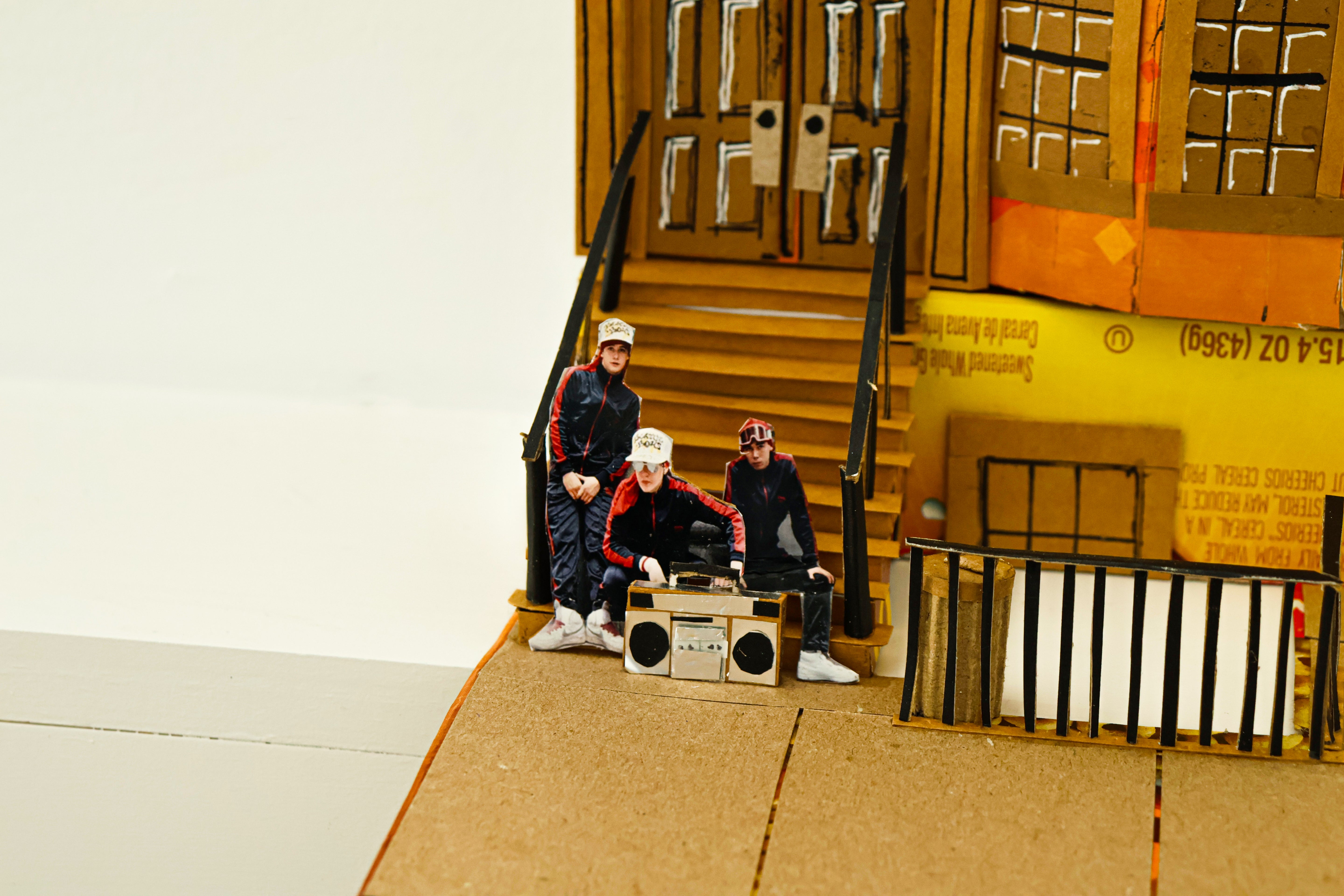 Model of a group of people with a boombox on a cardboard set with a door and boxes.